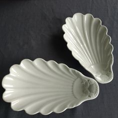 two white shell shaped dishes sitting on top of a black tablecloth covered table cloth