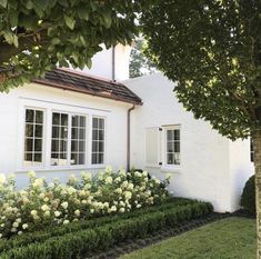 a white house with flowers in front of it and trees around the window sill