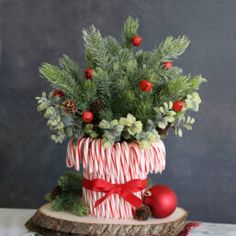 a vase filled with greenery and candy canes on top of a wooden slice