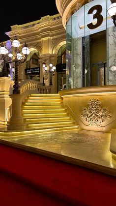 the stairs are lit up at night in front of an ornate building with columns and chandeliers