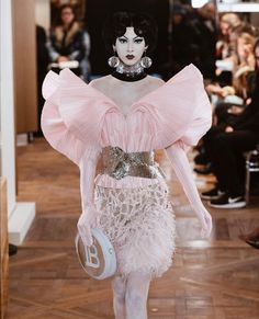 a model walks down the runway in a pink dress with feathers on her skirt and headpiece