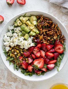 a white bowl filled with strawberries, cucumber, avocado and nuts