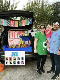 two adults and a child standing in front of a car with decorations on the trunk