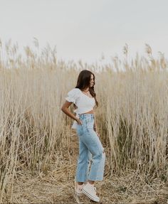 a woman standing in the middle of a field with her hands on her hips and looking off into the distance