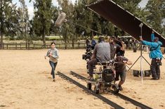 a group of people standing around a camera on top of a dirt field with trees in the background