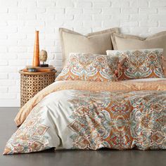 a bed with an orange and blue comforter next to a white brick wall in a bedroom