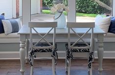 a dining room table with four chairs and a vase on top of it in front of a window