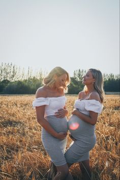 two pregnant women standing in a field with the sun shining down on their stomachs