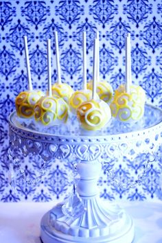 cake pops with yellow swirls are on a white stand in front of a blue and white wall