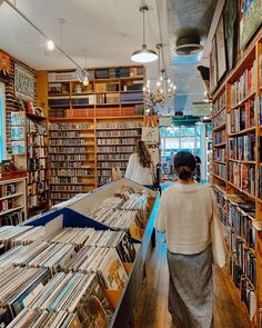 a woman is walking through a bookstore with many books on the shelves and people looking at them