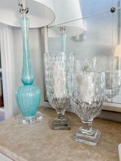 three glass vases sitting on top of a counter next to a lamp and mirror