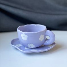 a purple cup and saucer with white flowers on it sitting on top of a table