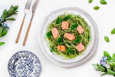 a white plate topped with pasta covered in salmon and greens next to a bowl of broccoli