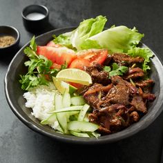 a bowl filled with meat, vegetables and rice on top of a black countertop