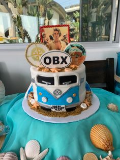 a blue and white bus cake sitting on top of a table covered in seashells