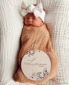 a baby wrapped in a blanket with a white headband and name on the side