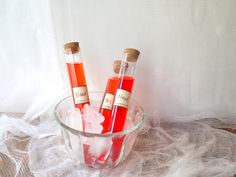 two bottles filled with red liquid sitting in a glass bowl on top of a table