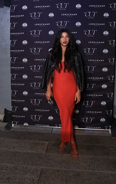 a woman standing in front of a wall wearing a red dress and black leather jacket