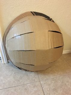 a large cardboard ball sitting on the floor next to a white wall and tile floor