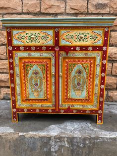 an ornately painted cabinet on display in front of a brick wall and cement floor