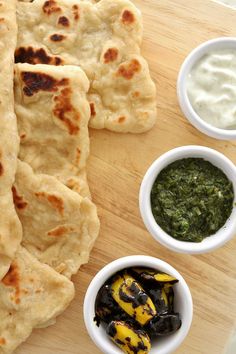 some pita breads are on a cutting board with dips and sauces