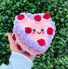 a hand holding a small crocheted heart with red and purple flowers on it