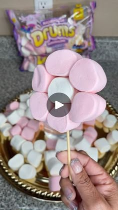 a person holding a flower shaped marshmallow lollipop in front of a plate of candy