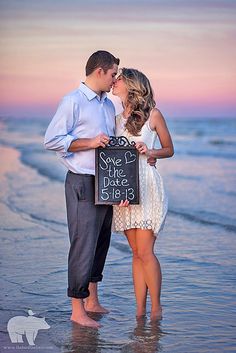 a couple kissing on the beach with a chalkboard sign in front of them that says save the date