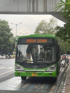 a green bus driving down a street next to a tall building with a sign that reads break down