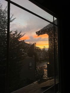 the sun is setting through an open window with rain drops on it and buildings in the background