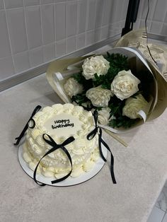 a birthday cake and bouquet of white roses on a counter