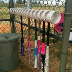 several baseball bats are hanging on a chain link fence near a trash can and garbage can