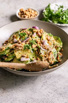 a salad in a bowl with wooden spoons on the side and other dishes around it