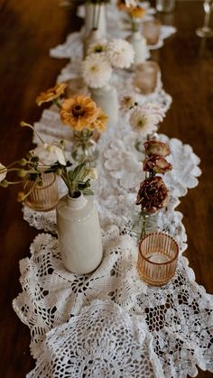 the table is covered with white doily and has flowers in vases on it