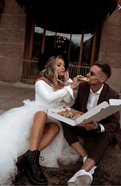 a man and woman sitting on the ground eating food from a box while wearing white dresses