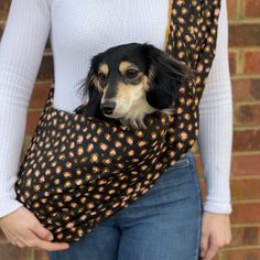 a woman holding a dog wrapped in a sling on her back while standing next to a brick wall