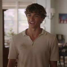 a young man with curly hair wearing a polo shirt and smiling at the camera in a living room