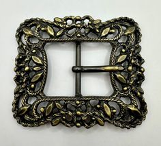 a metal belt buckle with leaves and vines on the front, attached to a white wall