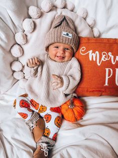 a baby laying on top of a bed next to a pillow with the words more pumpkin written on it