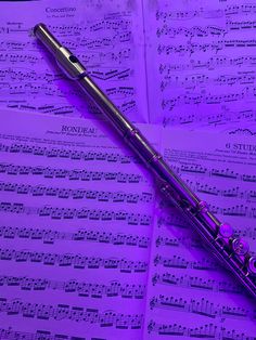 a flute laying on top of sheet music with purple lights in the room behind it