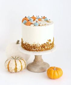 there is a white cake with gold sprinkles on it and two small pumpkins next to it