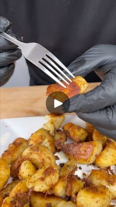 a person in black gloves is holding a fork over some food on a white plate