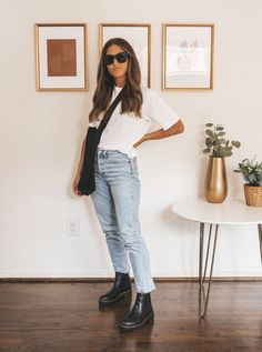 ashley wearing a white tee, light was mom jeans, black lug sole Chelsea boots, and a black mesh tote bag; in the background, a white round side table with 2 plants and 3 prints in gold frames on a white wall Casual Fall Concert Outfits, London Style 2023, Casual Jean Work Outfits, Straight Legged Jeans Outfits, 80 Degree Weather Outfits Fall, 80 Degree Weather Outfits, How To Style Chelsea Boots