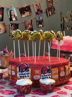 taco cake and cupcakes are displayed on a table in front of pictures