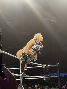 a female wrestler standing on top of a metal pole in the middle of a ring