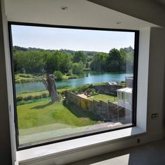 a large window with a view of a river and trees outside it, in front of a white wall