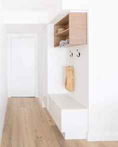 an empty hallway with white walls and wooden flooring on the other side, there is a coat rack in the corner