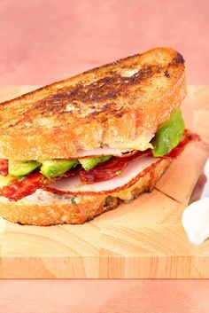 a toasted sandwich with meat, lettuce and tomato on a cutting board