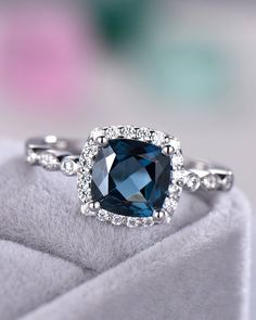 a cushion cut blue diamond surrounded by white diamonds on top of a velvet ring box