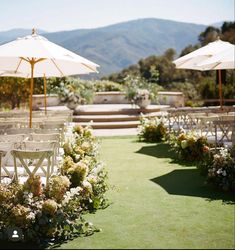 an outdoor ceremony set up with white chairs and umbrellas